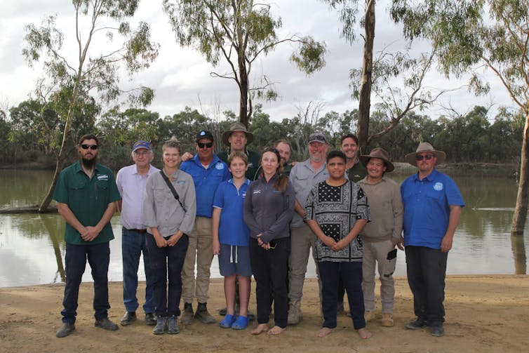 A group of 13 people standing on the banks of the Murray River in South Australia, the team responsible for the Murray crayfish reintroduction program.